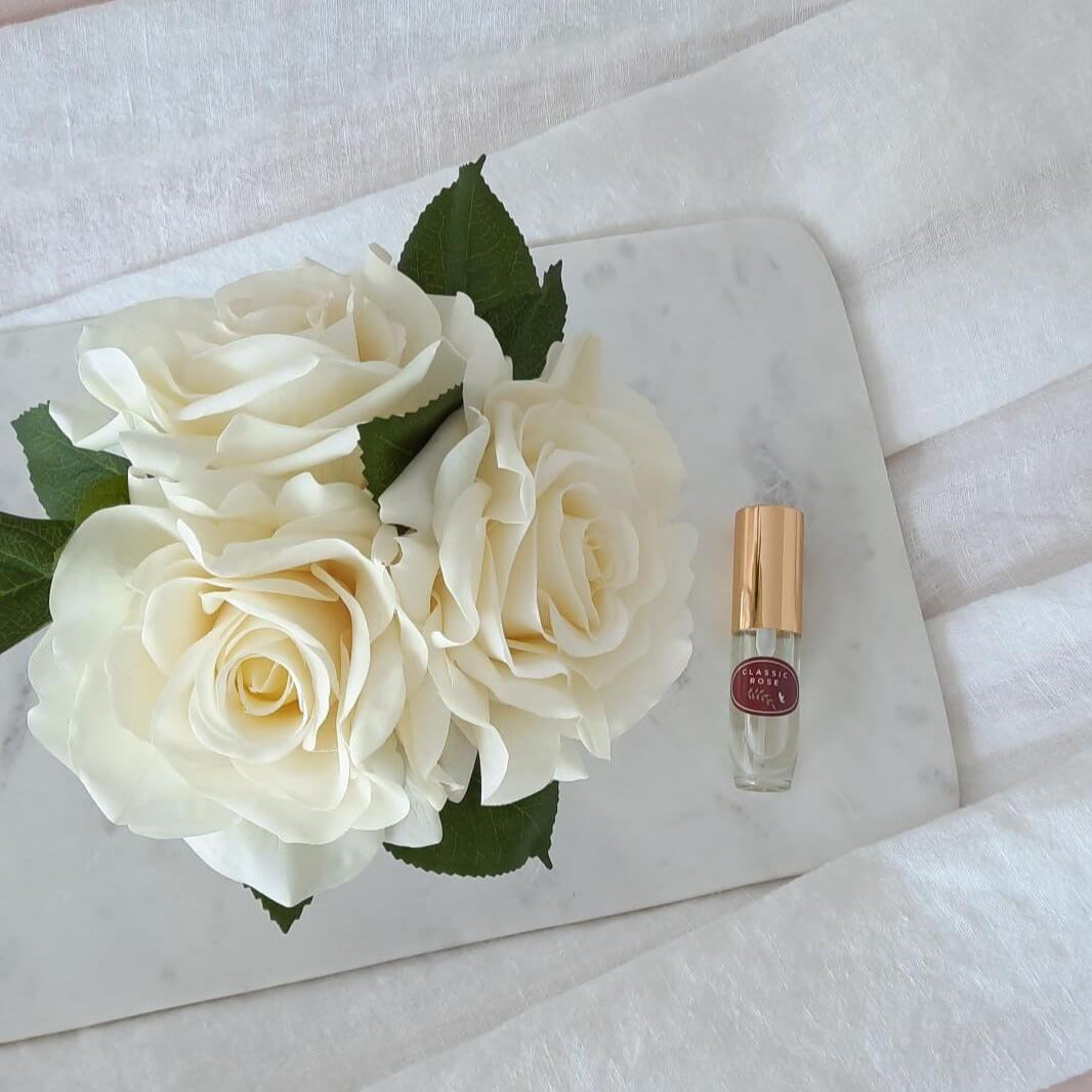 3 artificial white roses arranged in a glass vase paired with a classic rose fragrance spray